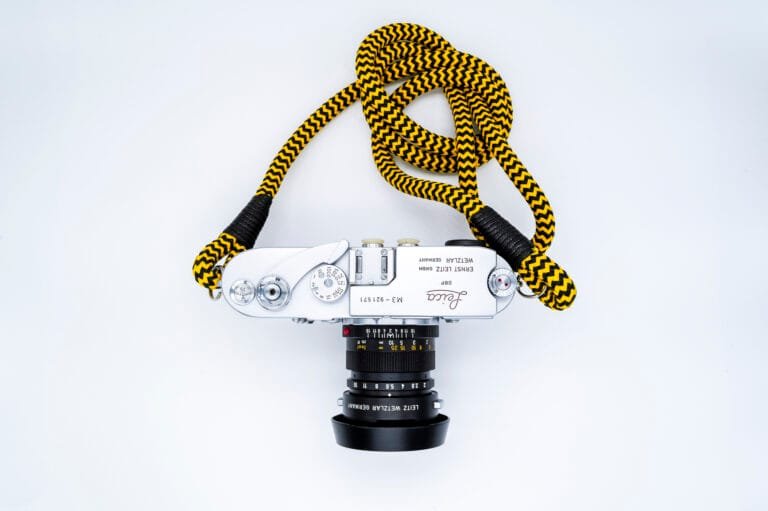 Leica M3 vu de dessus avec un objectif Leitz Summicron et une sangle jaune et noire, posé sur fond blanc.
