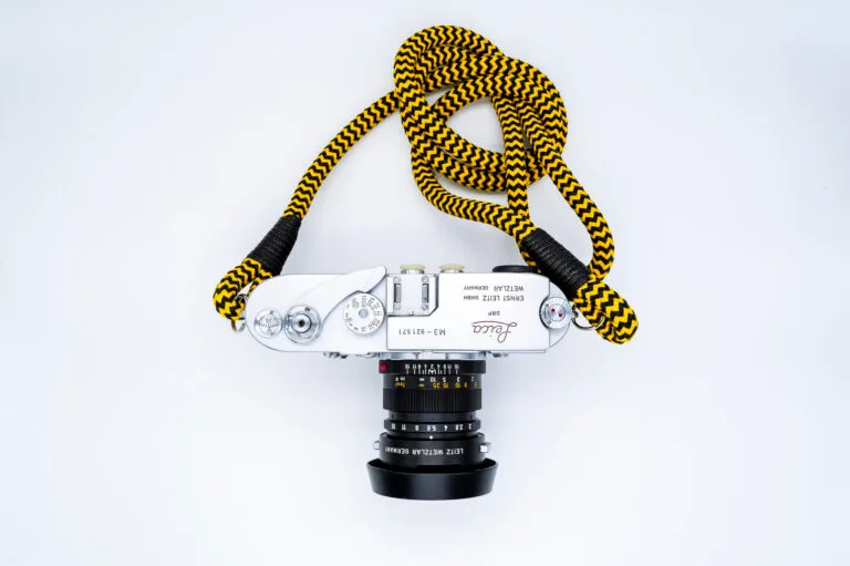 Leica M3 vu de dessus avec un objectif Leitz Summicron et une sangle jaune et noire, posé sur fond blanc.