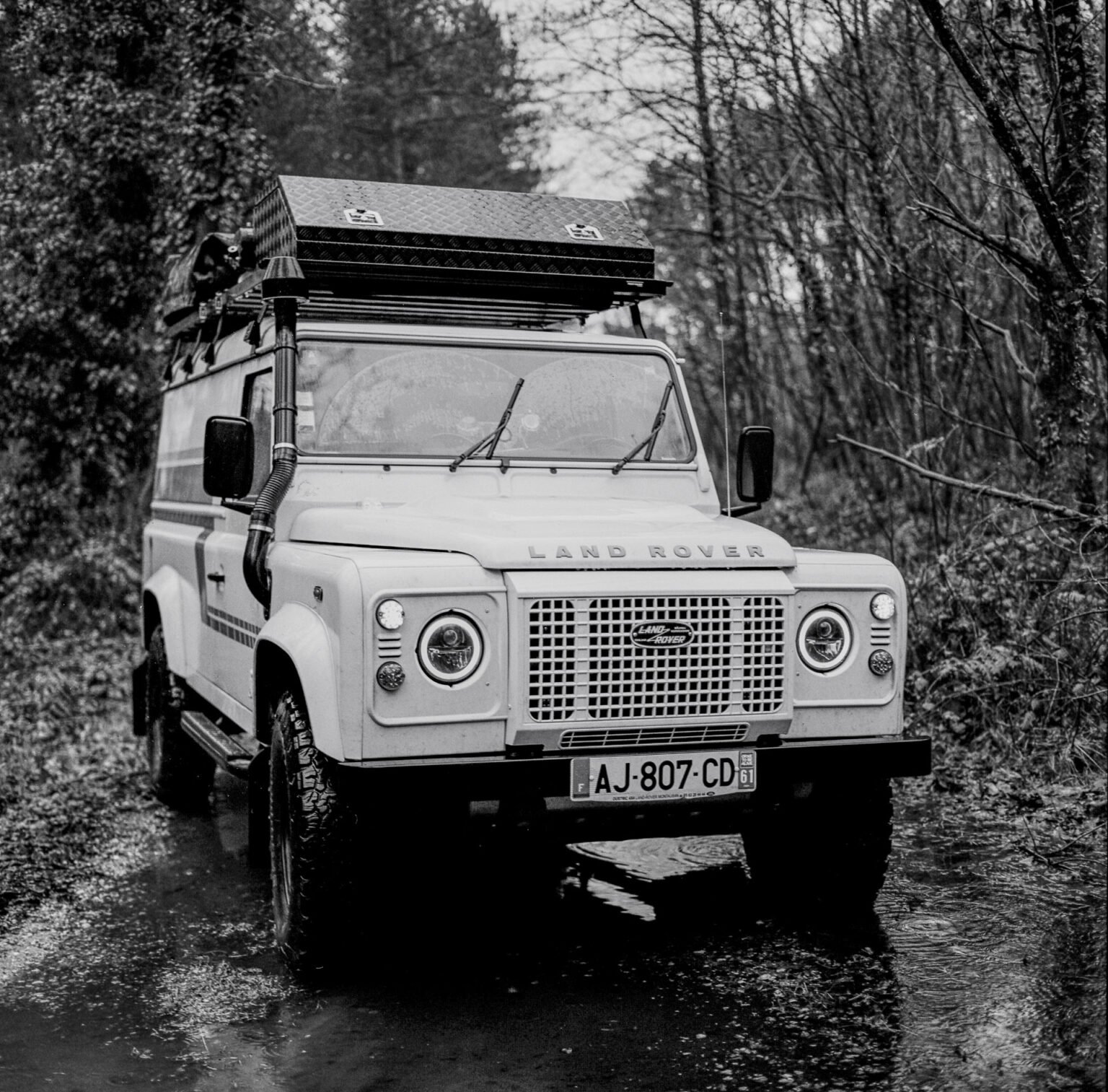 Land Rover Defender stationné sur un chemin forestier boueux près du Mans, photographié en noir et blanc avec un Hasselblad 500 C/M.