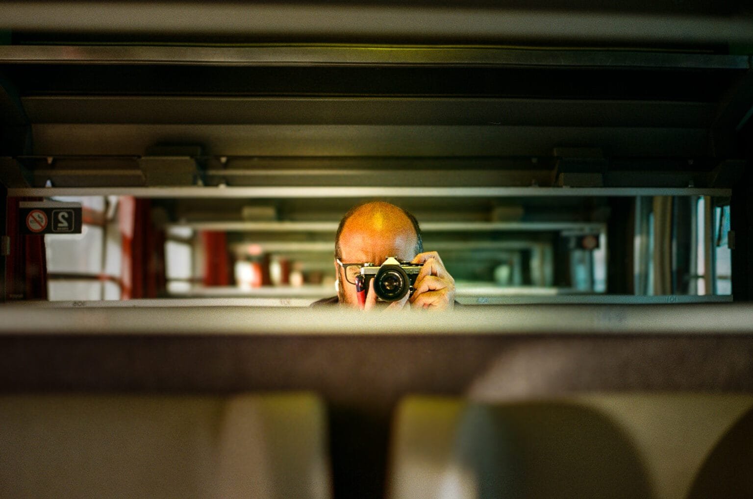 Autoportrait pris dans un train, reflet dans un miroir, appareil Olympus OM-2 en main.