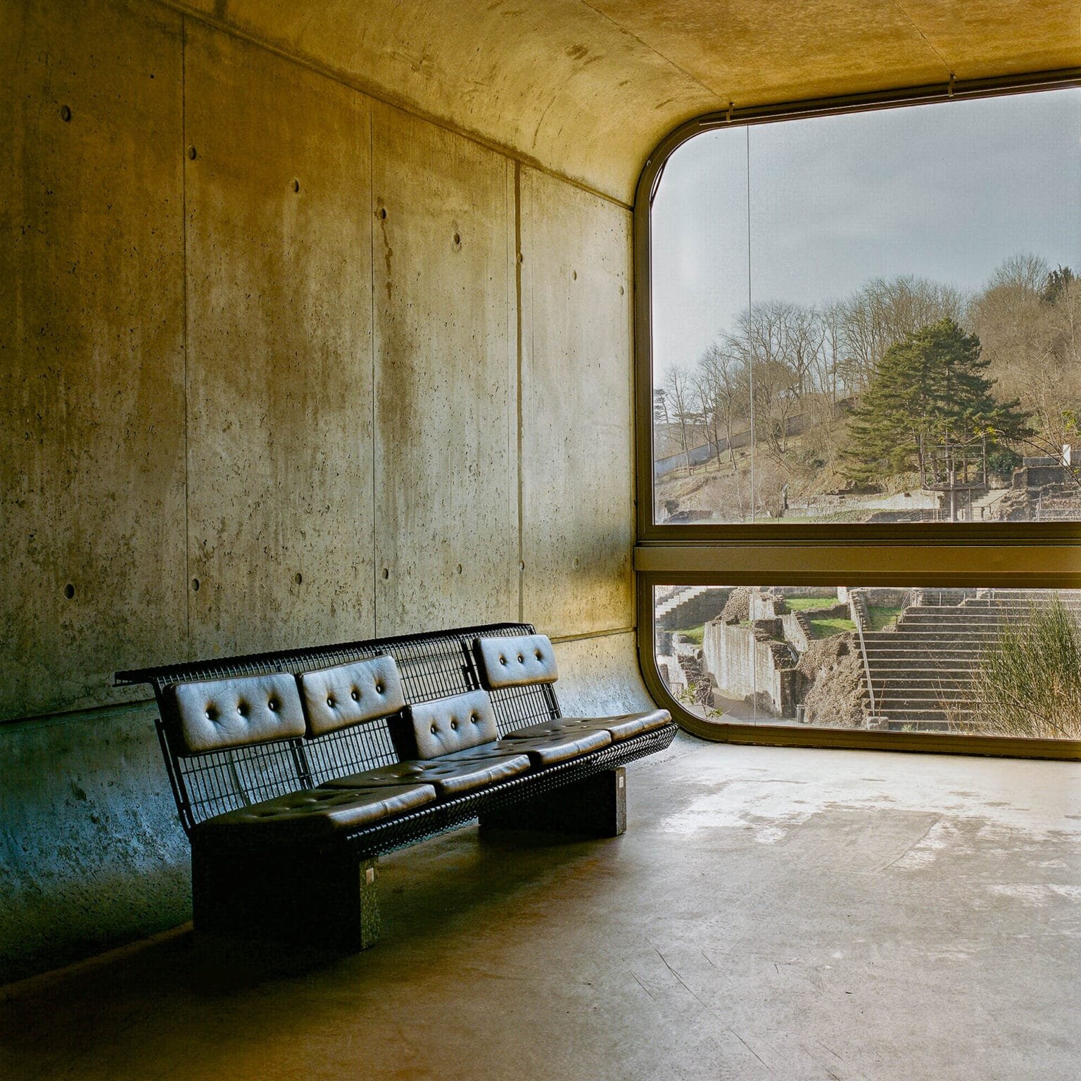 Banc en cuir et métal dans le musée Lugdunum à Lyon, face à une grande baie vitrée surplombant le site archéologique des théâtres romains.