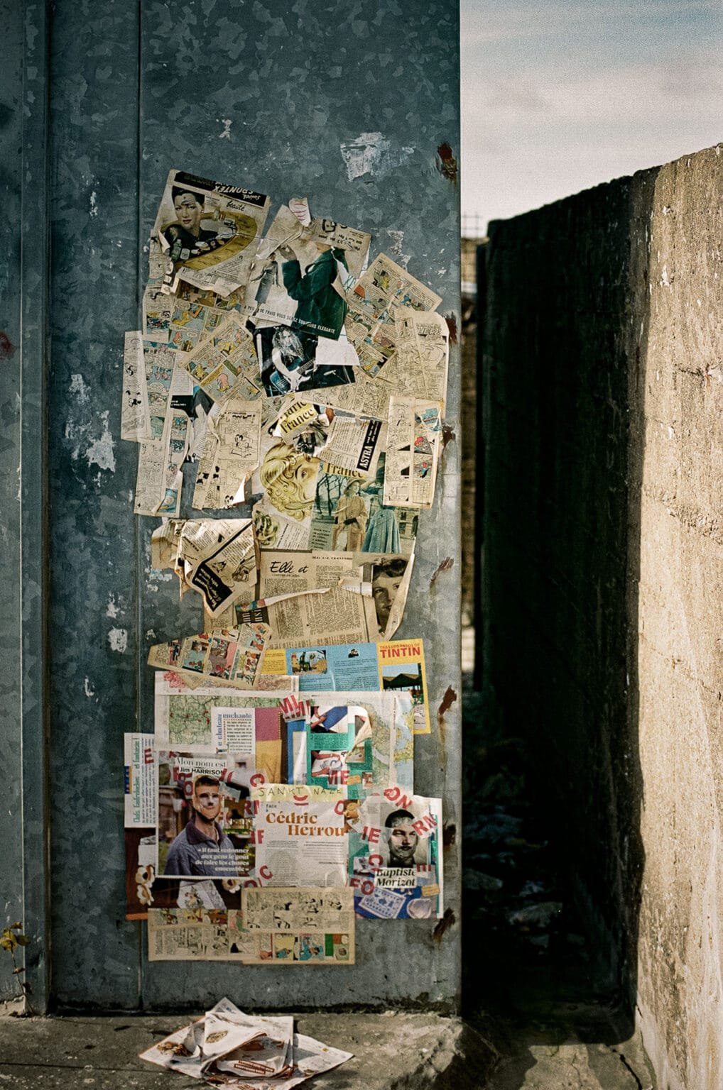 Mur de la base sous-marine de Saint-Nazaire recouvert de collages de journaux, de bandes dessinées et d’affiches anciennes, photographié en couleur.