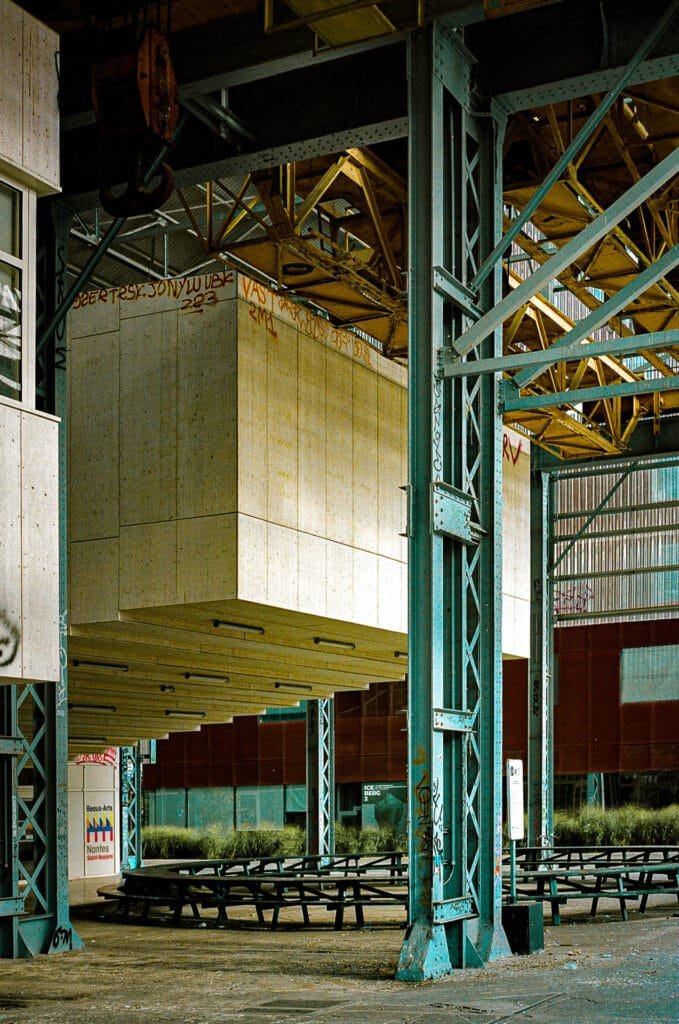 Structures métalliques et modules suspendus à l’école des Beaux-Arts de Nantes, avec des bancs en bois en contrebas.