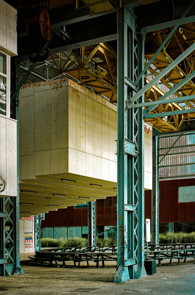 Structures métalliques et modules suspendus à l’école des Beaux-Arts de Nantes, avec des bancs en bois en contrebas.