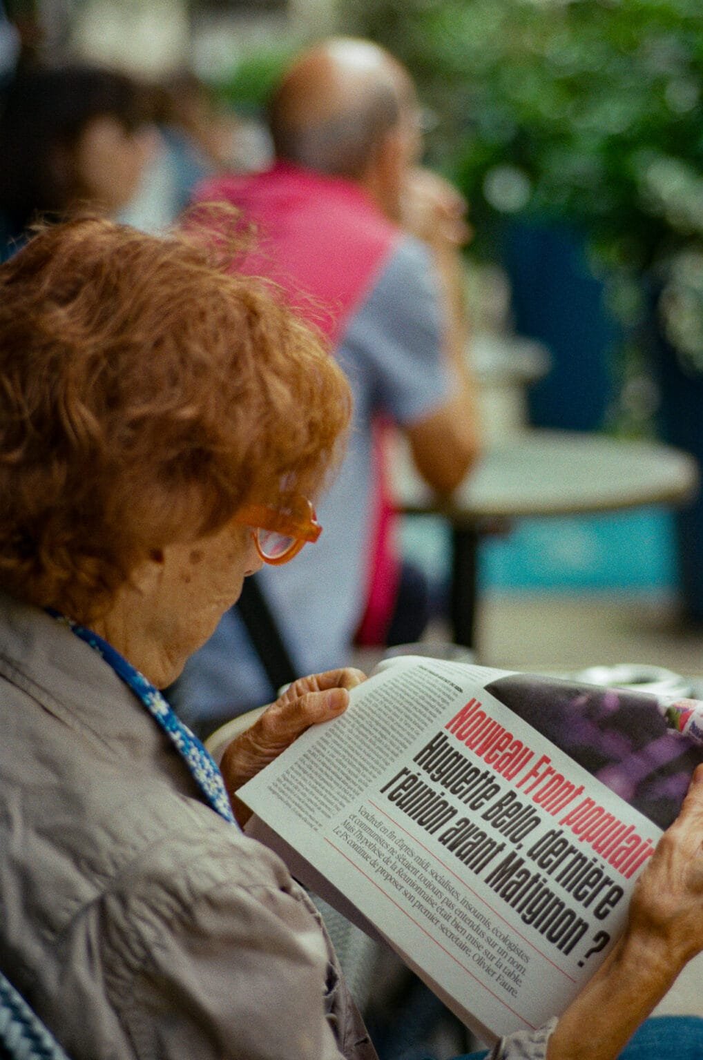 Femme aux cheveux roux lisant un journal sur le Nouveau Front Populaire en terrasse du café Aristide à Nantes.