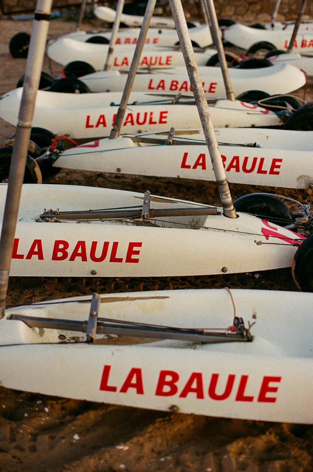 Alignement de chars à voile blancs marqués “La Baule” sur le sable au lever du soleil.