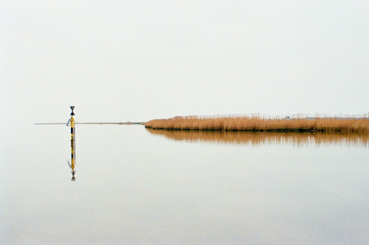 Vue minimaliste sur la Loire à Cordemais avec un balisage maritime et des roseaux se reflétant dans l’eau calme.