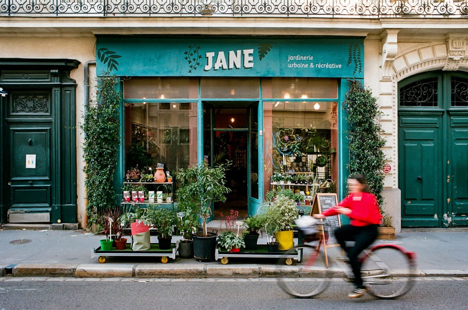 Femme à vélo passant devant la boutique Jane à Nantes, spécialisée en jardinage urbain.