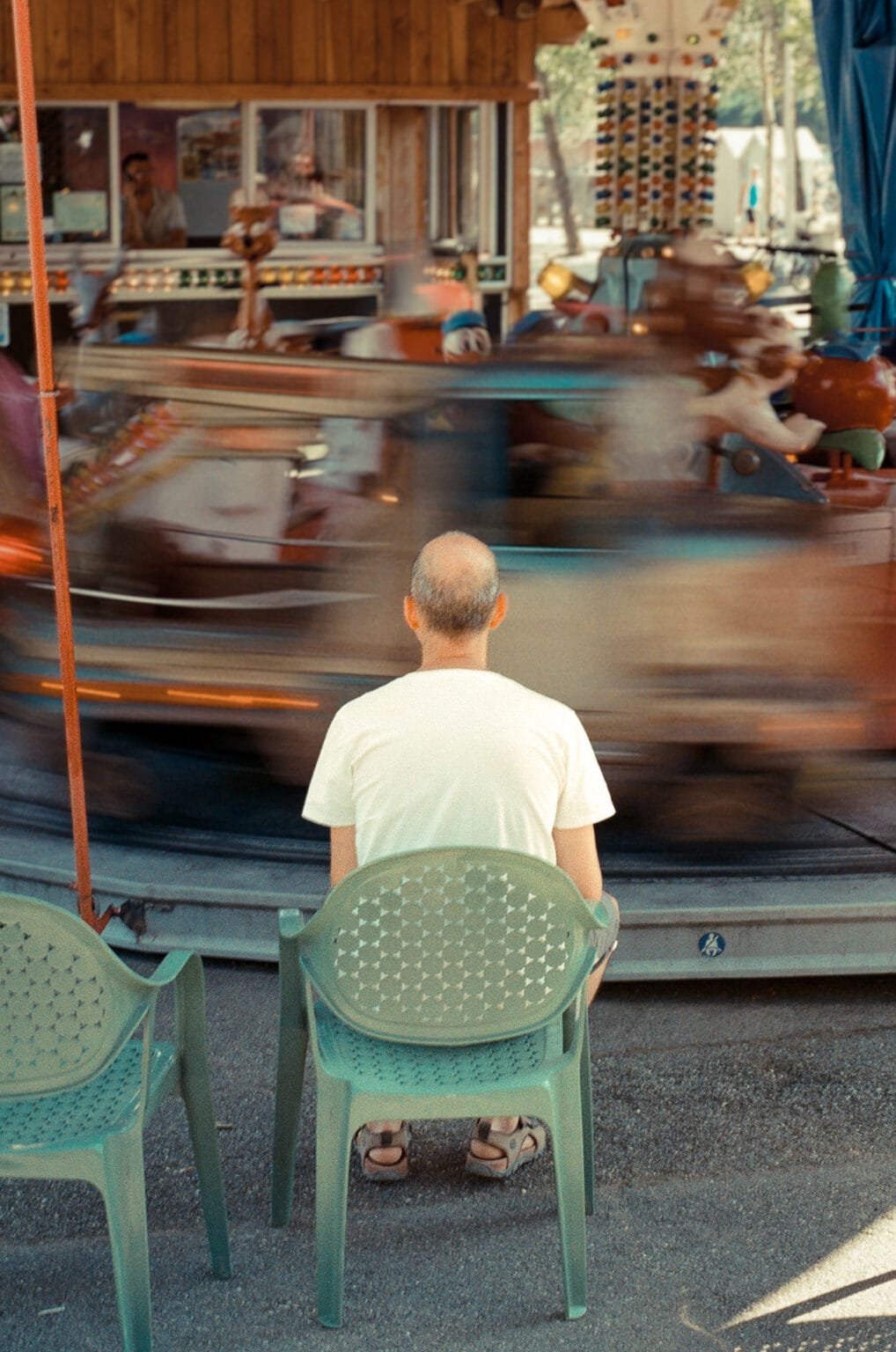 Homme assis face à un manège en mouvement, près de la plage d’Embrun.