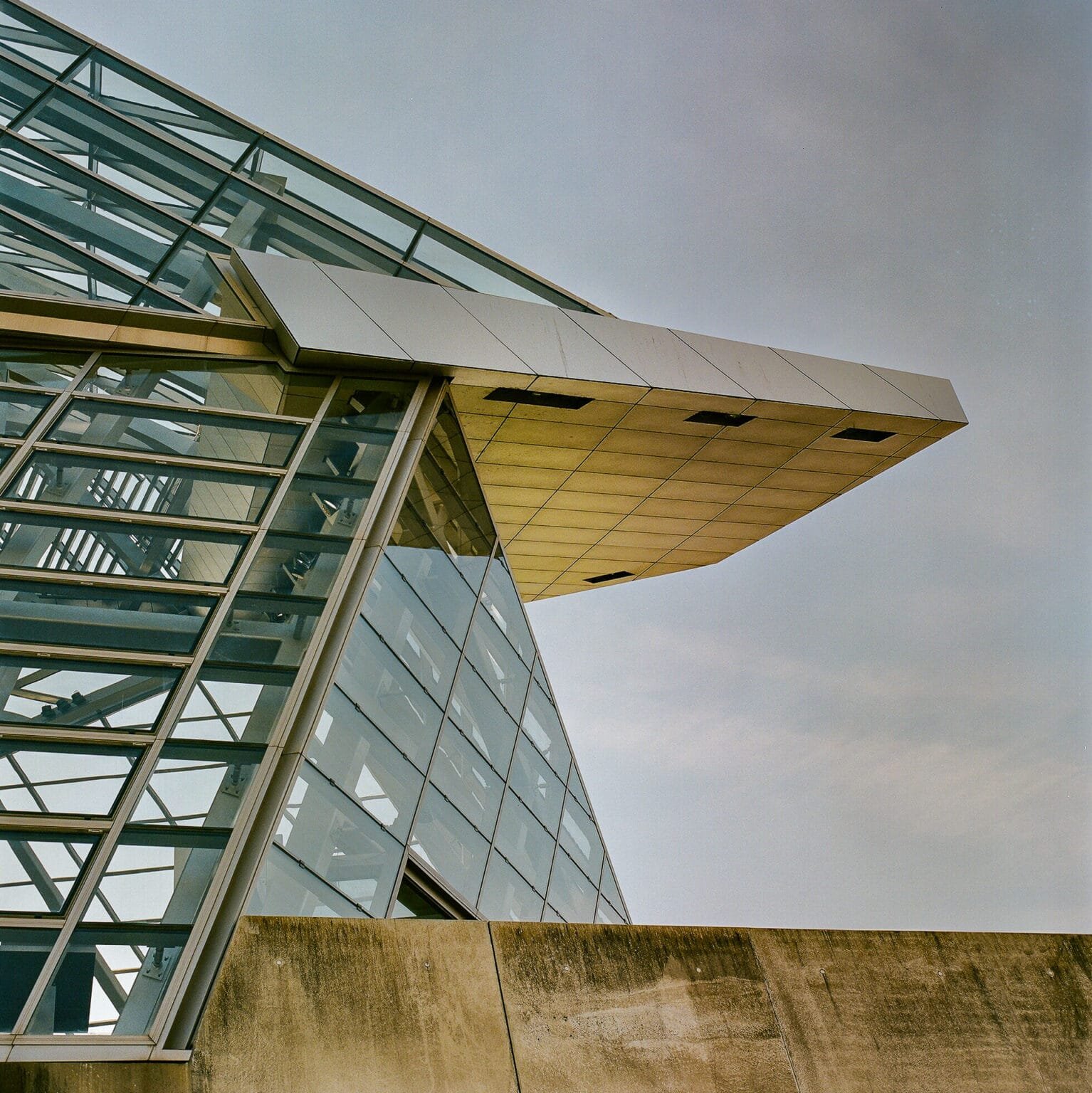 Détail architectural de la façade vitrée du musée des Confluences à Lyon, capturé en contre-plongée avec une lumière douce de fin de journée.