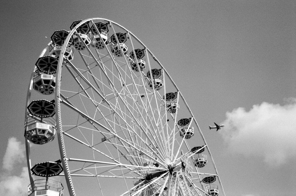 Grande roue de la fête foraine de Nantes en noir et blanc, avec un avion en arrière-plan dans le ciel.