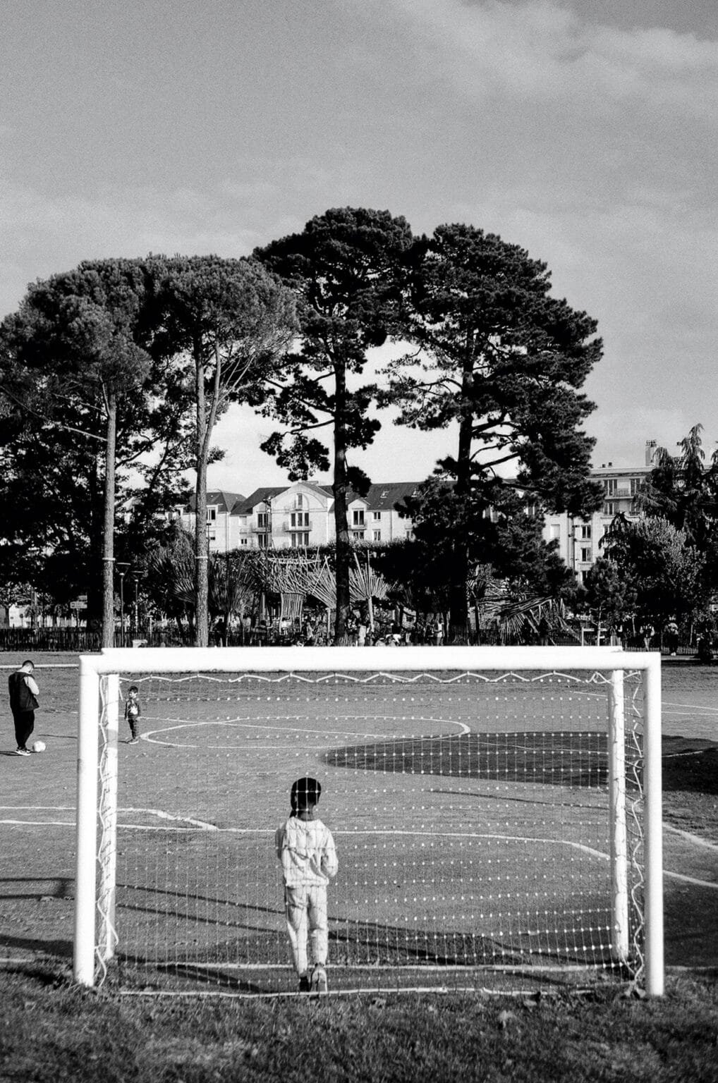 Un enfant vu de dos, dans un but de football sur le terrain du Feydball à Nantes, en noir et blanc.