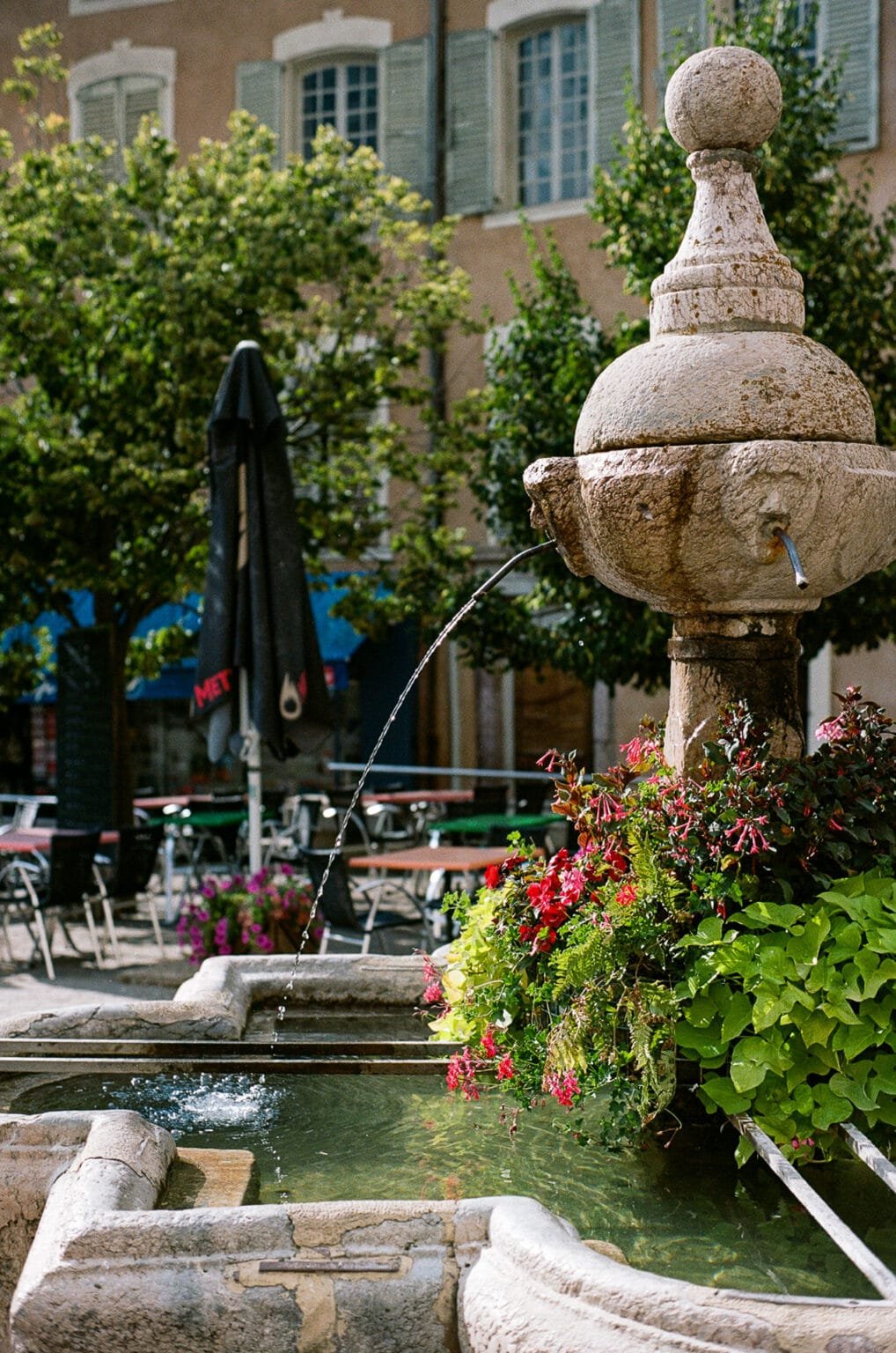 Fontaine en pierre avec fleurs colorées sur la place du village d’Embrun.