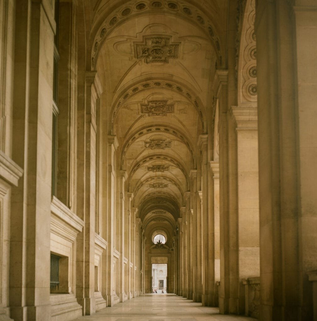 Galerie voûtée du Louvre à Paris, avec ses arches et ses ornements sculptés en pierre, photographiée en lumière naturelle sur pellicule Portra 160.