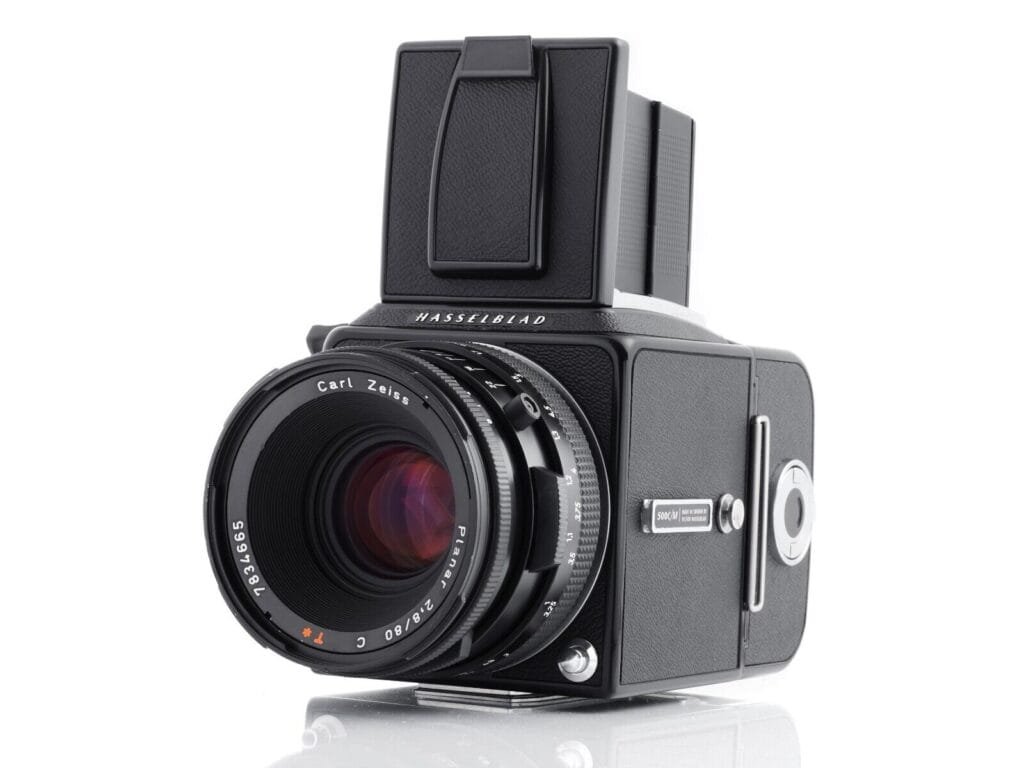 Hasselblad 500 C/M équipé d’un objectif Carl Zeiss Planar 80mm f/2.8, photographié en vue de trois-quarts arrière gauche avec viseur poitrine relevé.