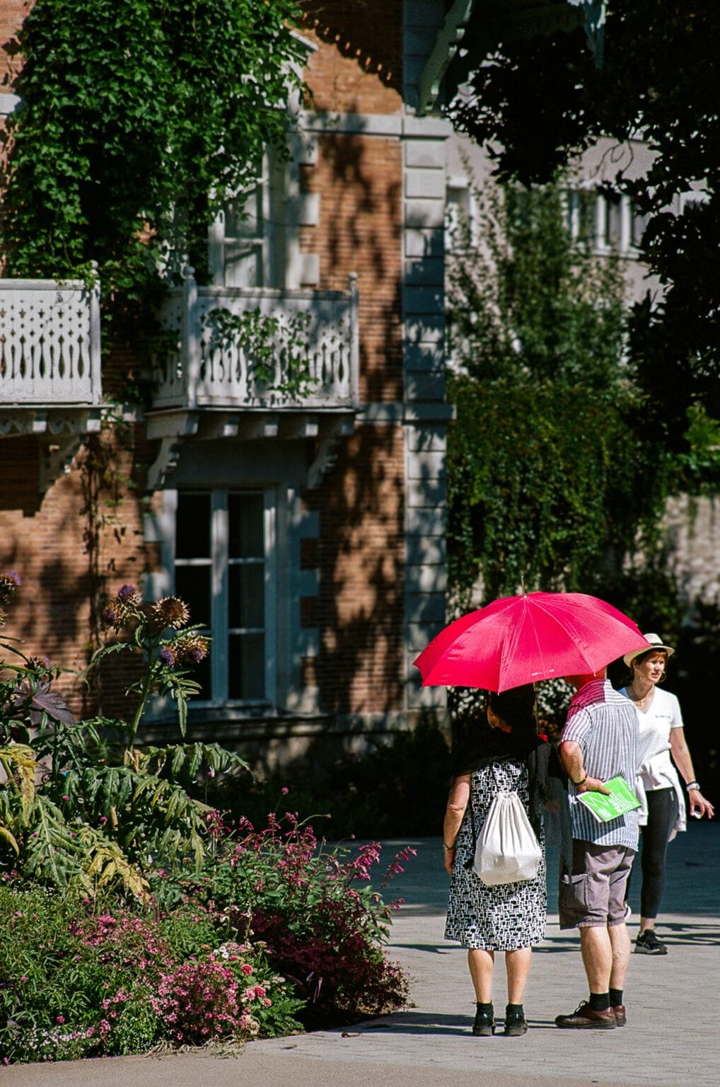 Couple sous un parapluie rouge au Jardin des Plantes de Nantes, devant une maison en briques.