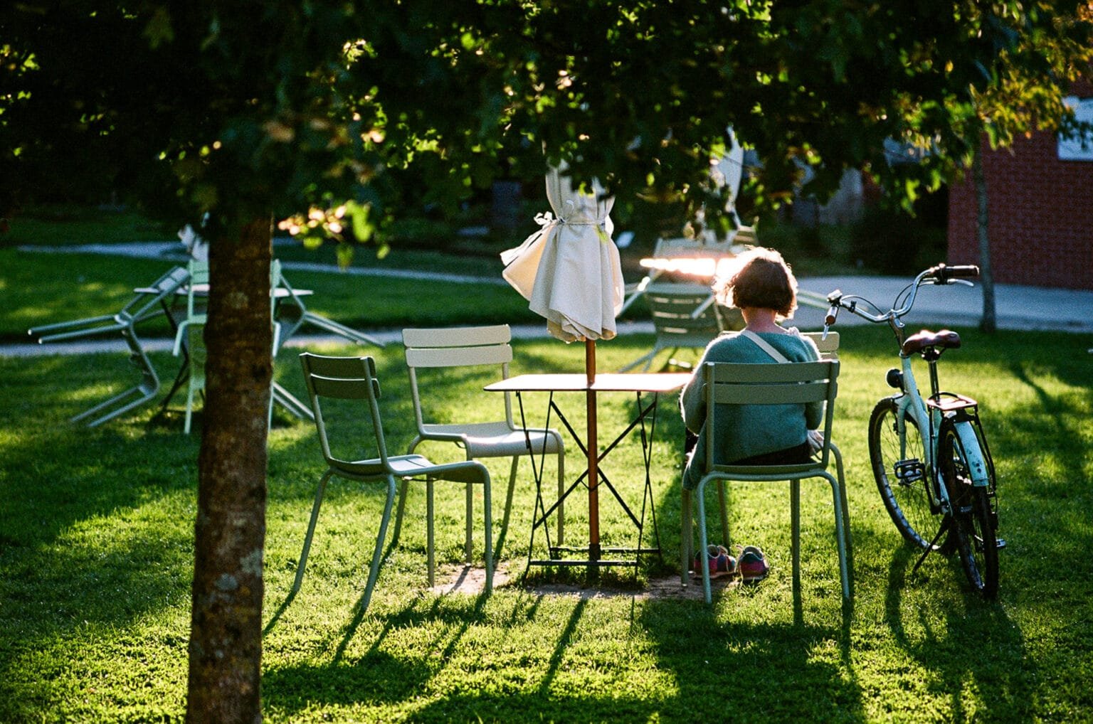 Femme assise à une table en métal vert dans le Jardin des Plantes, son vélo posé à côté.