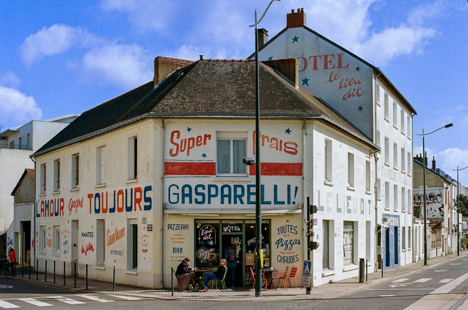 Façade colorée de l’établissement Le Lieu Dit à Nantes, avec des inscriptions peintes sur les murs et une terrasse animée.