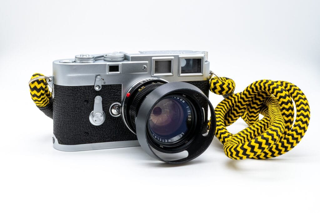 Leica M3 de 1958 avec un objectif Summicron 50mm f/2 monté et une dragonne jaune et noire, présenté en vue de trois quarts.