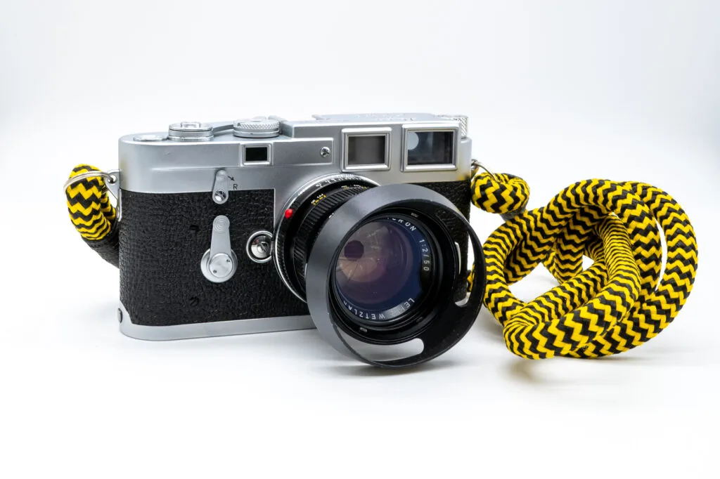 Leica M3 de 1958 avec un objectif Summicron 50mm f/2 monté et une dragonne jaune et noire, présenté en vue de trois quarts.