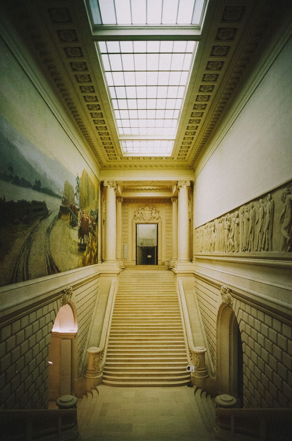 Grand escalier en pierre du Musée d’Arts de Nantes encadré de fresques et bas-reliefs.