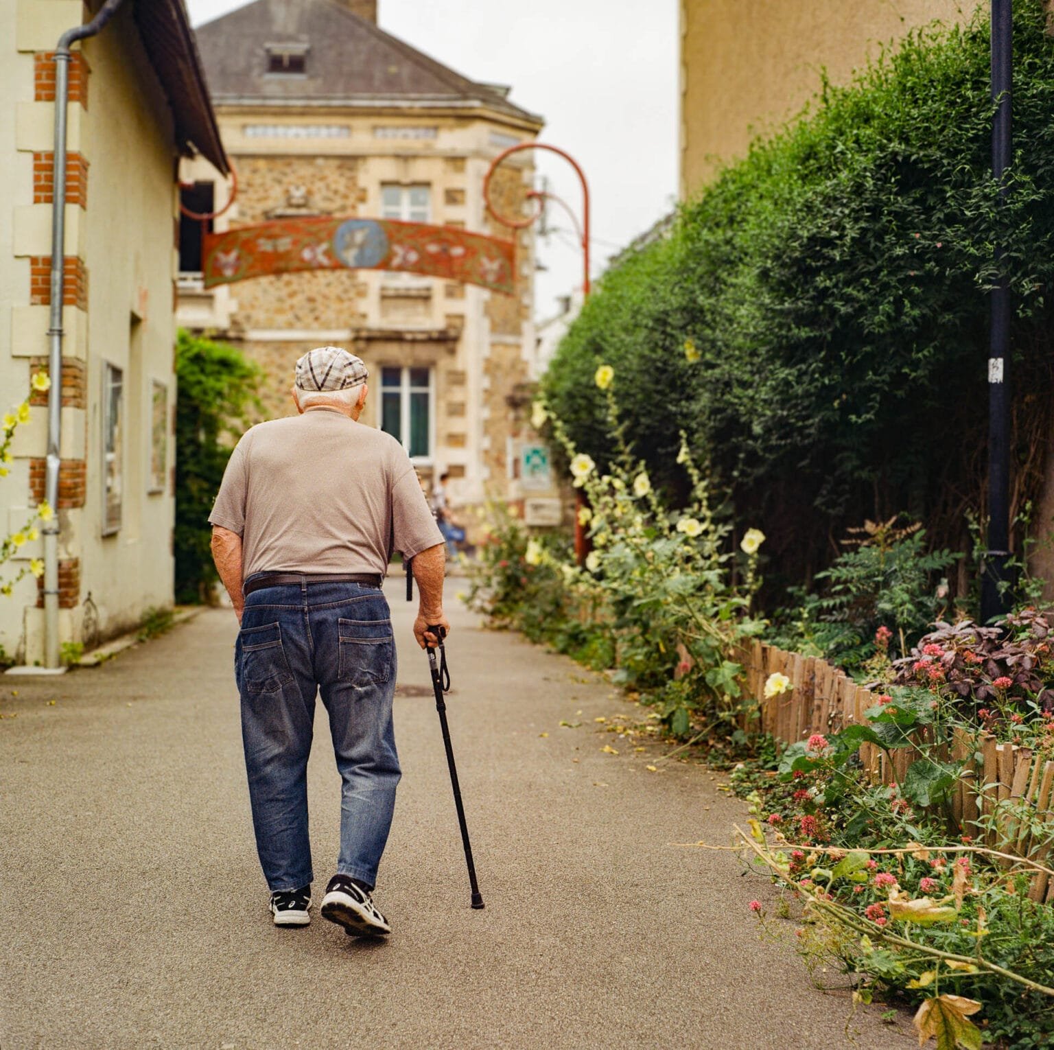 Homme âgé marchant avec une canne dans une ruelle fleurie de Nantes en été.
