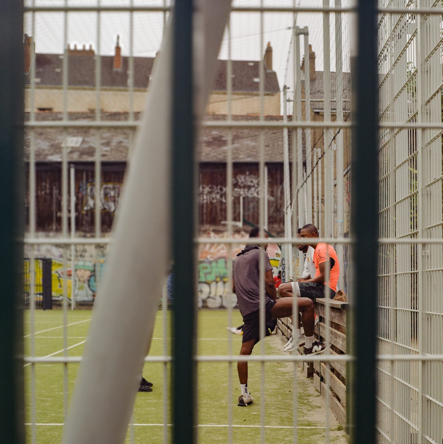 Jeunes discutant dans un city stade grillagé à Nantes, graffitis en arrière-plan.
