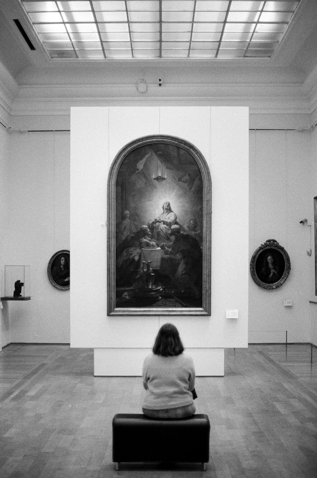 Personne assise devant un grand tableau au Palais des Beaux-Arts de Lille, contemplant l’œuvre dans une salle d’exposition, photo en noir et blanc.