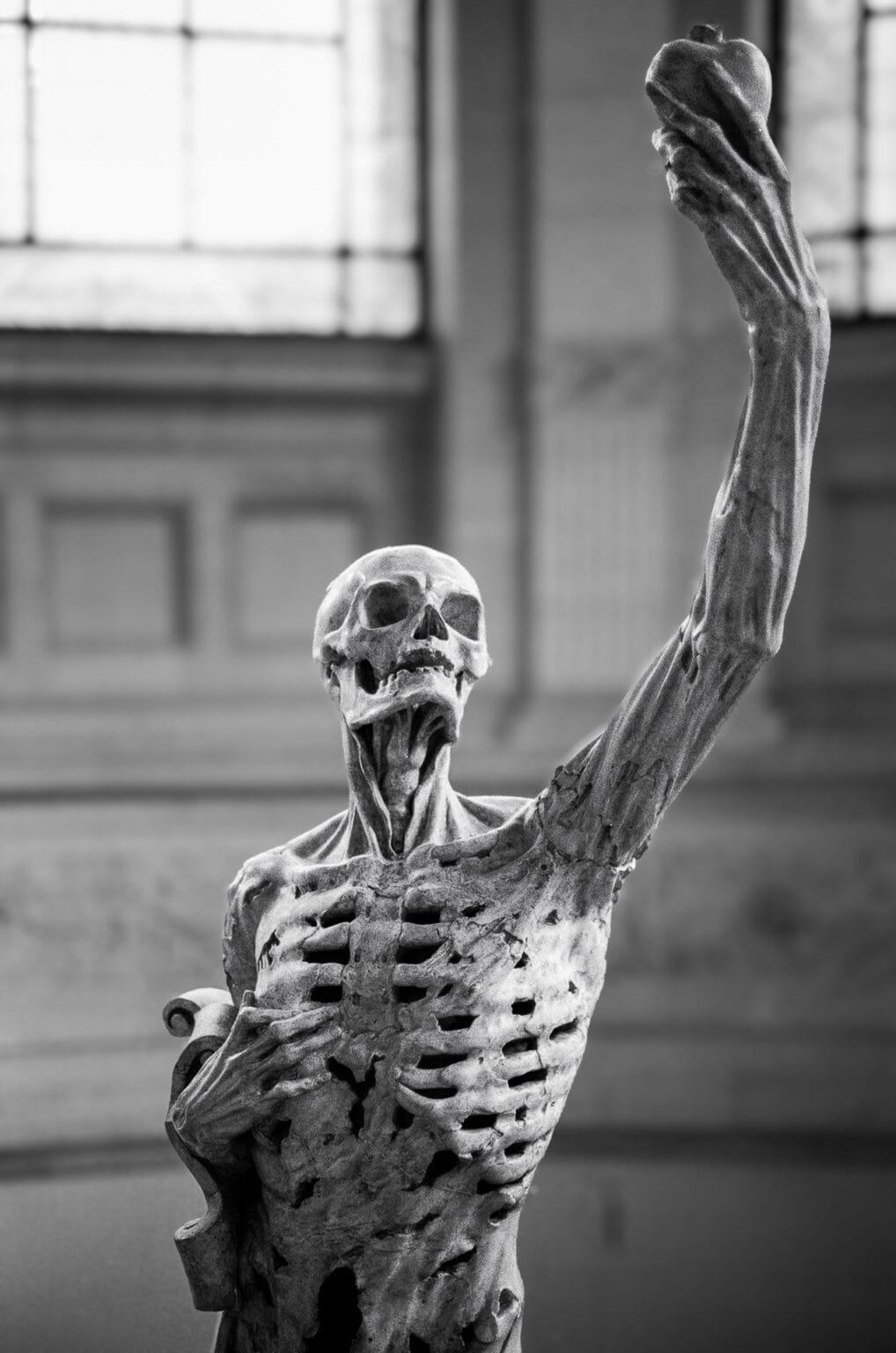 Statue Le Transi de Pompon exposée au Palais des Beaux-Arts de Lille, représentant un squelette tendant une pomme. Photographie en noir et blanc.