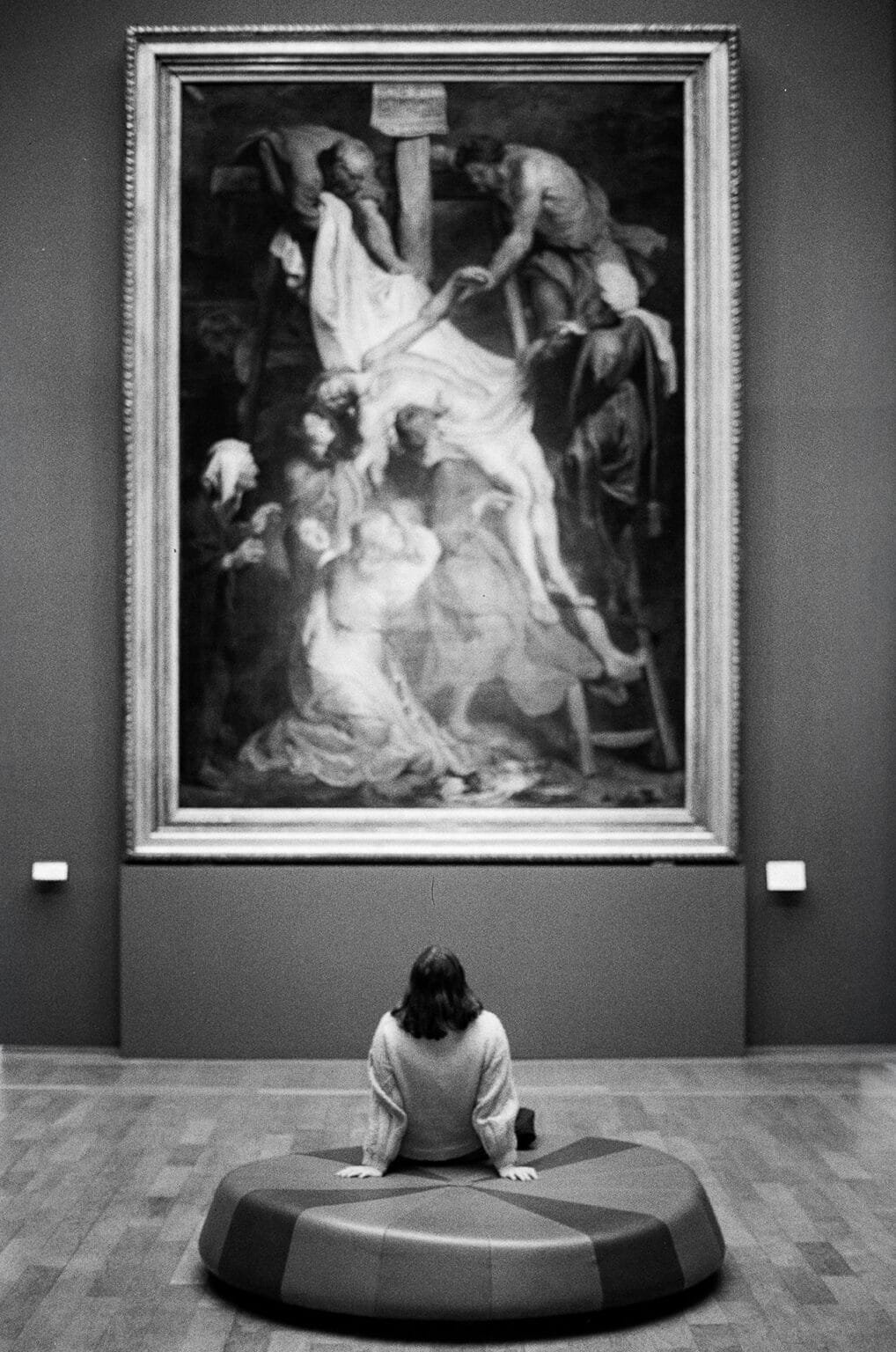 Personne assise devant un grand tableau religieux au Palais des Beaux-Arts de Lille, photo en noir et blanc.