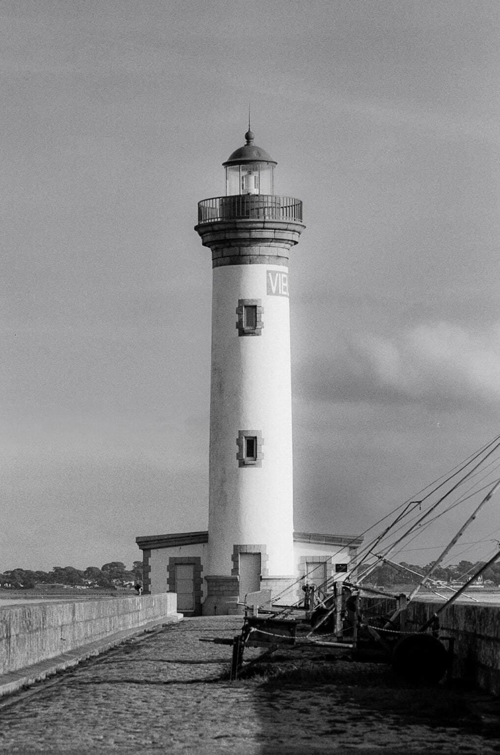 Le phare de Saint-Nazaire photographié en noir et blanc, vu depuis la jetée, avec des filets de pêche au premier plan.