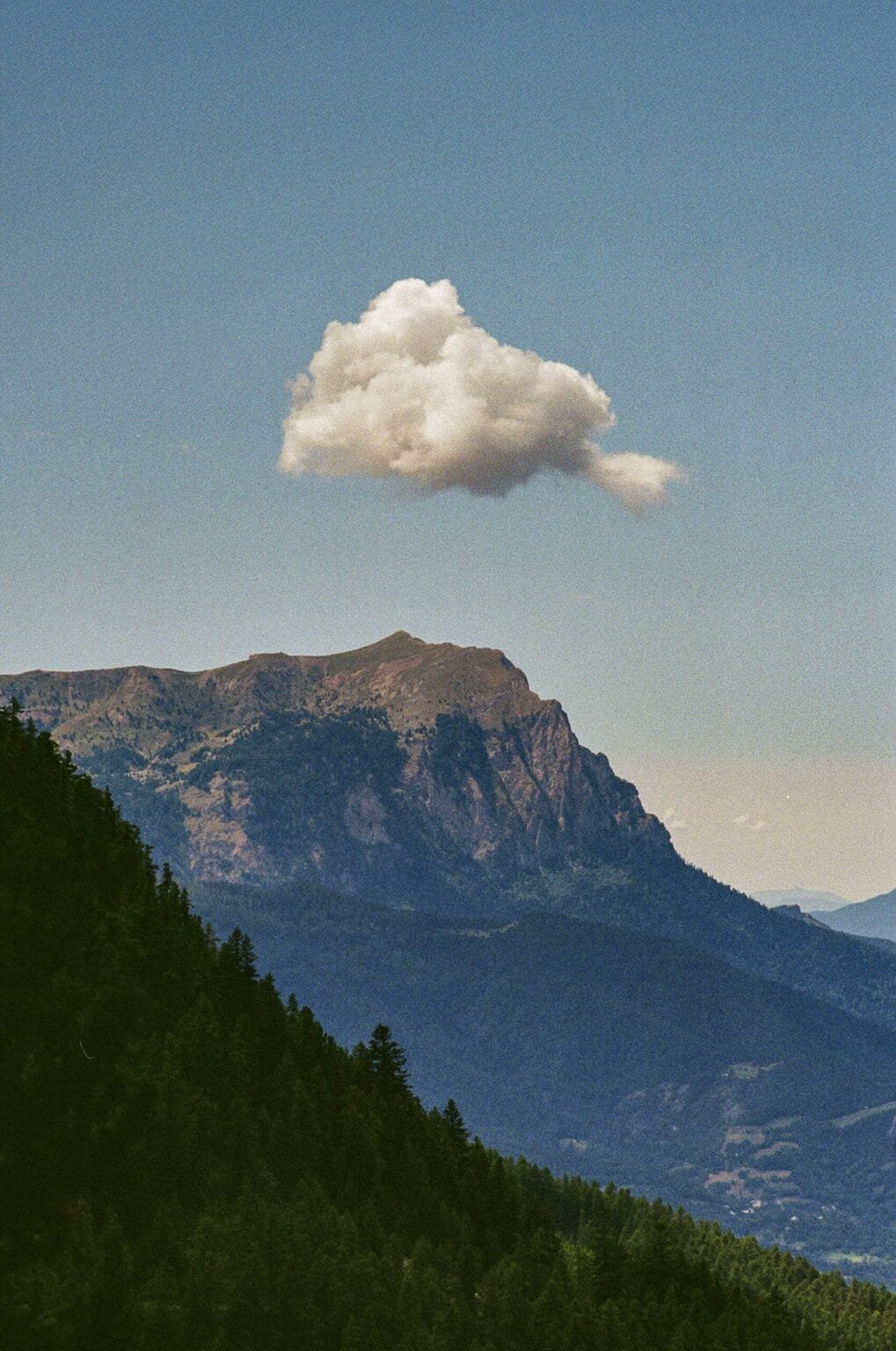 Le pic du Morgon vu depuis la vallée, avec un nuage solitaire dans le ciel bleu.