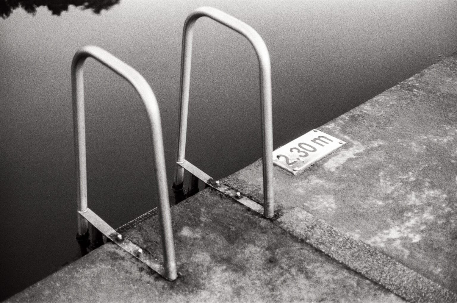 Échelle de piscine en métal plongeant dans l’eau sombre de la piscine du Prieuré à Dinard, panneau indiquant 2,30 m de profondeur.