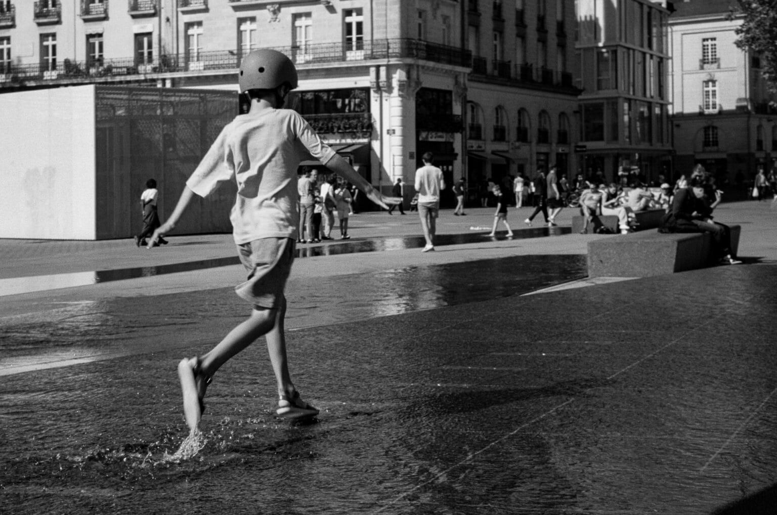 Enfant courant pieds nus dans les jeux d’eau de la place du Commerce à Nantes par une chaude journée d’été.