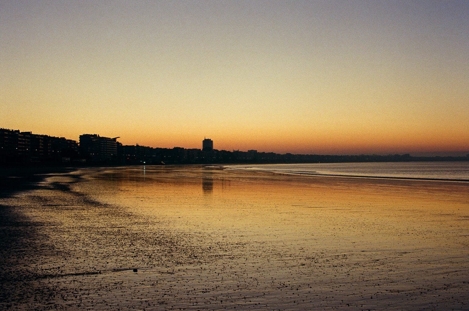 Lever du soleil sur la plage de La Baule, reflets dorés sur le sable humide et silhouette des immeubles en contre-jour.