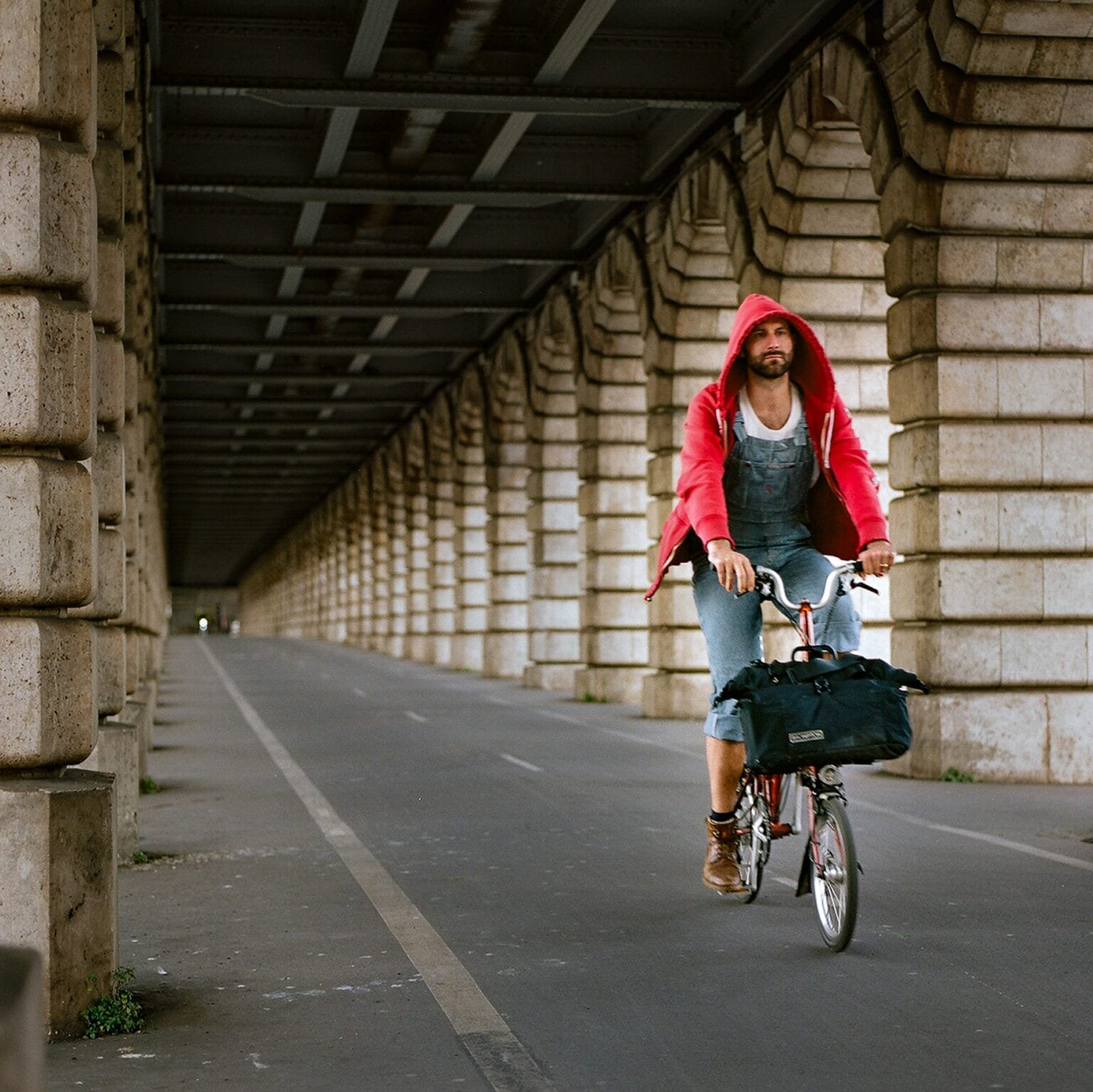 Cycliste en salopette et sweat rouge circulant sur la piste cyclable du Pont de Bercy à Paris.