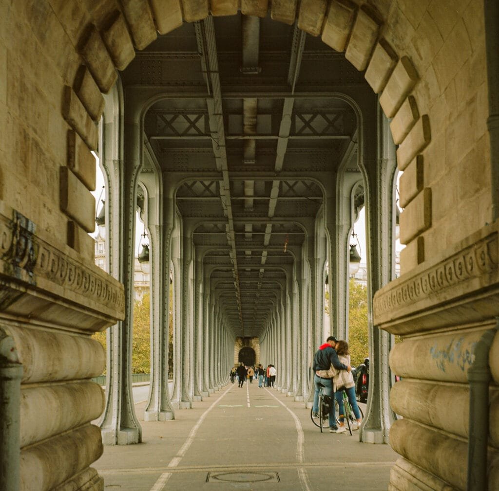Vue centrale du pont de Bir-Hakeim à Paris, capturée en format carré avec un Yashica Mat 124G sur pellicule Kodak Portra 160. Des piétons et cyclistes traversent le pont sous ses arches métalliques.