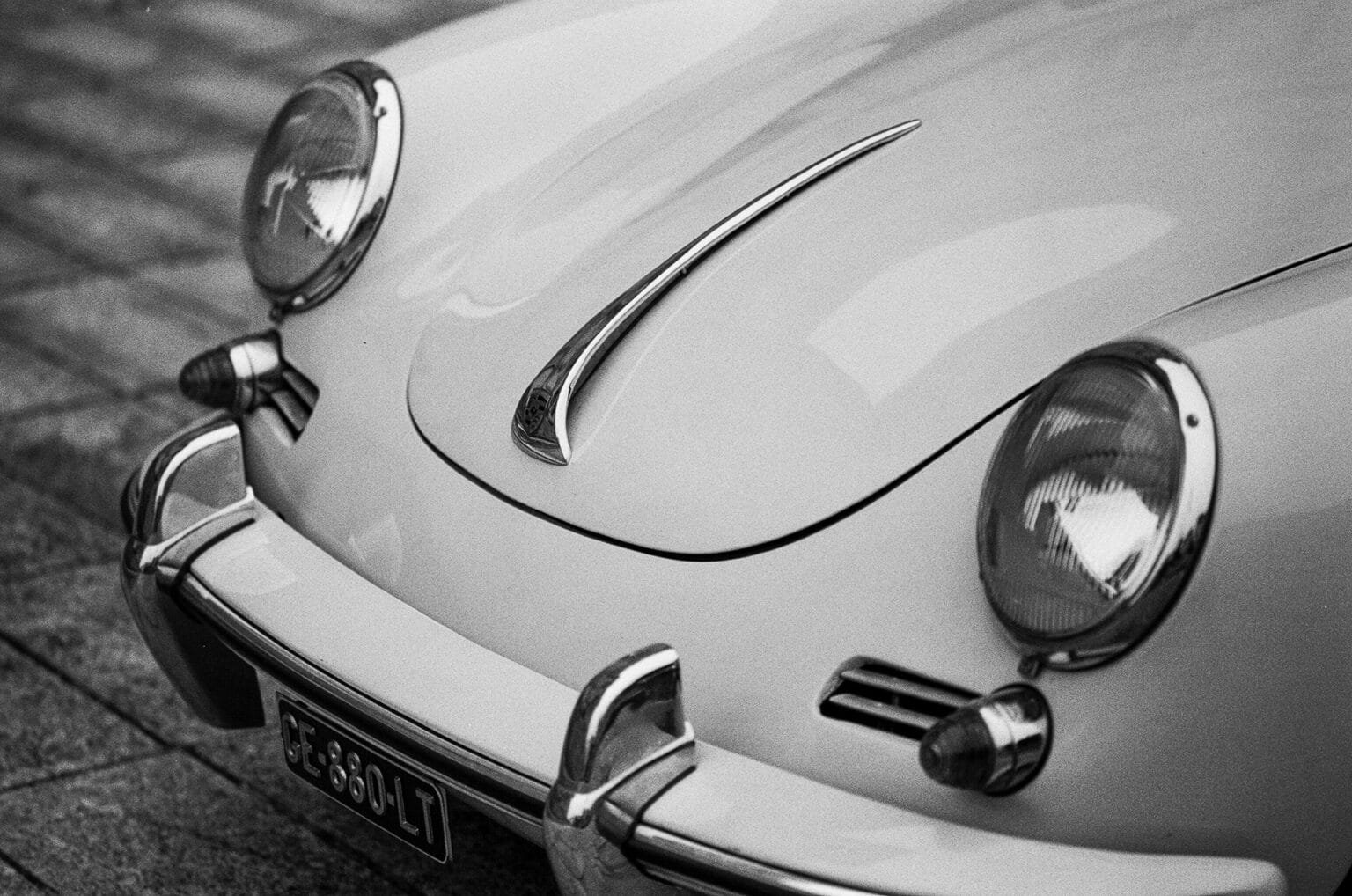Détail de la calandre avant d’une Porsche 356, avec vue sur les phares et l’emblème, photographiée en noir et blanc.