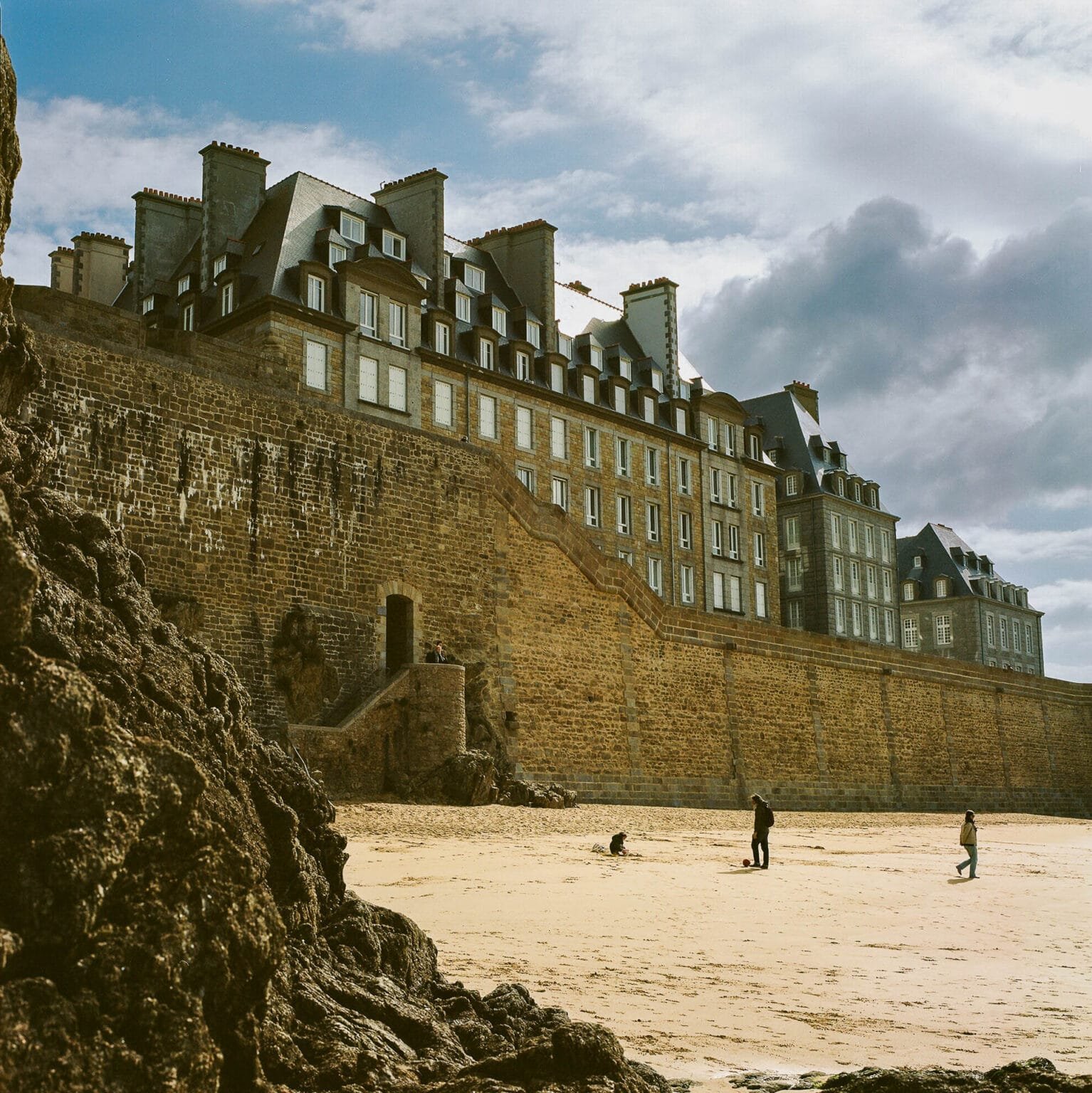 Les remparts et immeubles de Saint-Malo vus depuis la plage, sous un ciel nuageux.