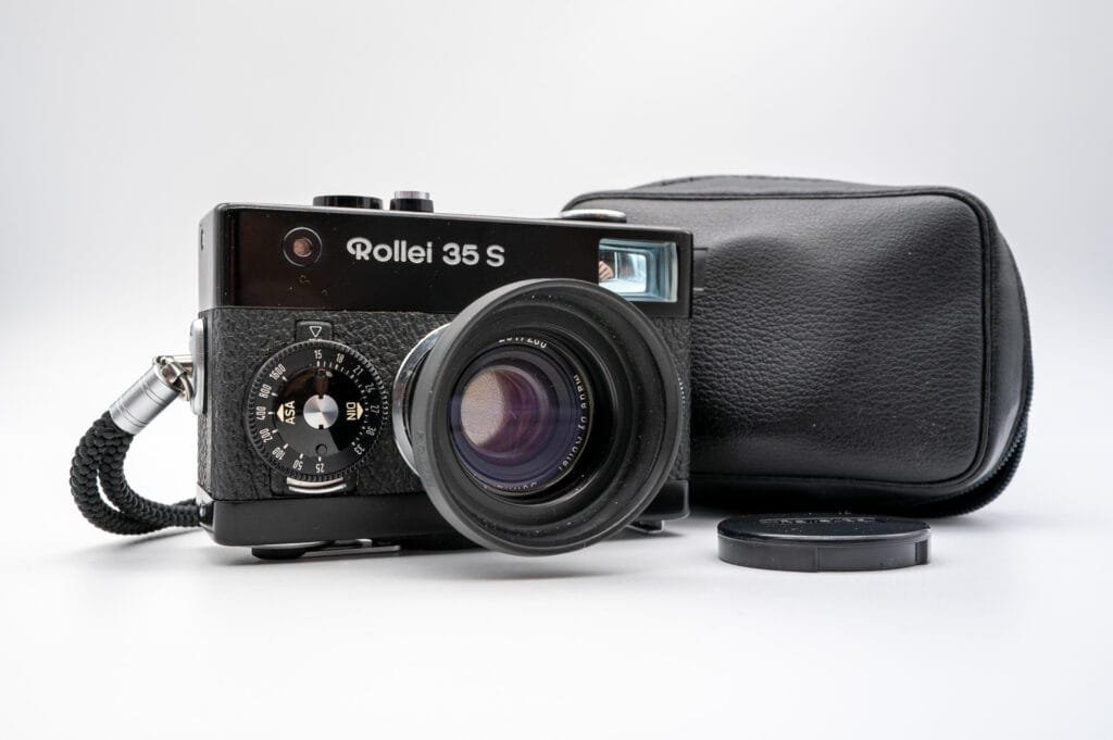 Rollei 35 S avec son objectif Sonnar 40mm f/2.8 déployé, accompagné de son étui en cuir noir et de son bouchon d’objectif.
