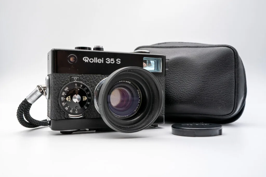 Rollei 35 S avec son objectif Sonnar 40mm f/2.8 déployé, accompagné de son étui en cuir noir et de son bouchon d’objectif.