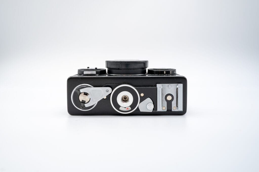 Vue du dessous du Rollei 35 S, montrant la manivelle de rembobinage, le pas de vis pour trépied et le sabot de flash.