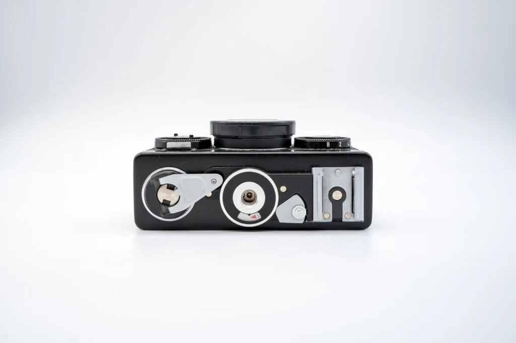 Vue du dessous du Rollei 35 S, montrant la manivelle de rembobinage, le pas de vis pour trépied et le sabot de flash.