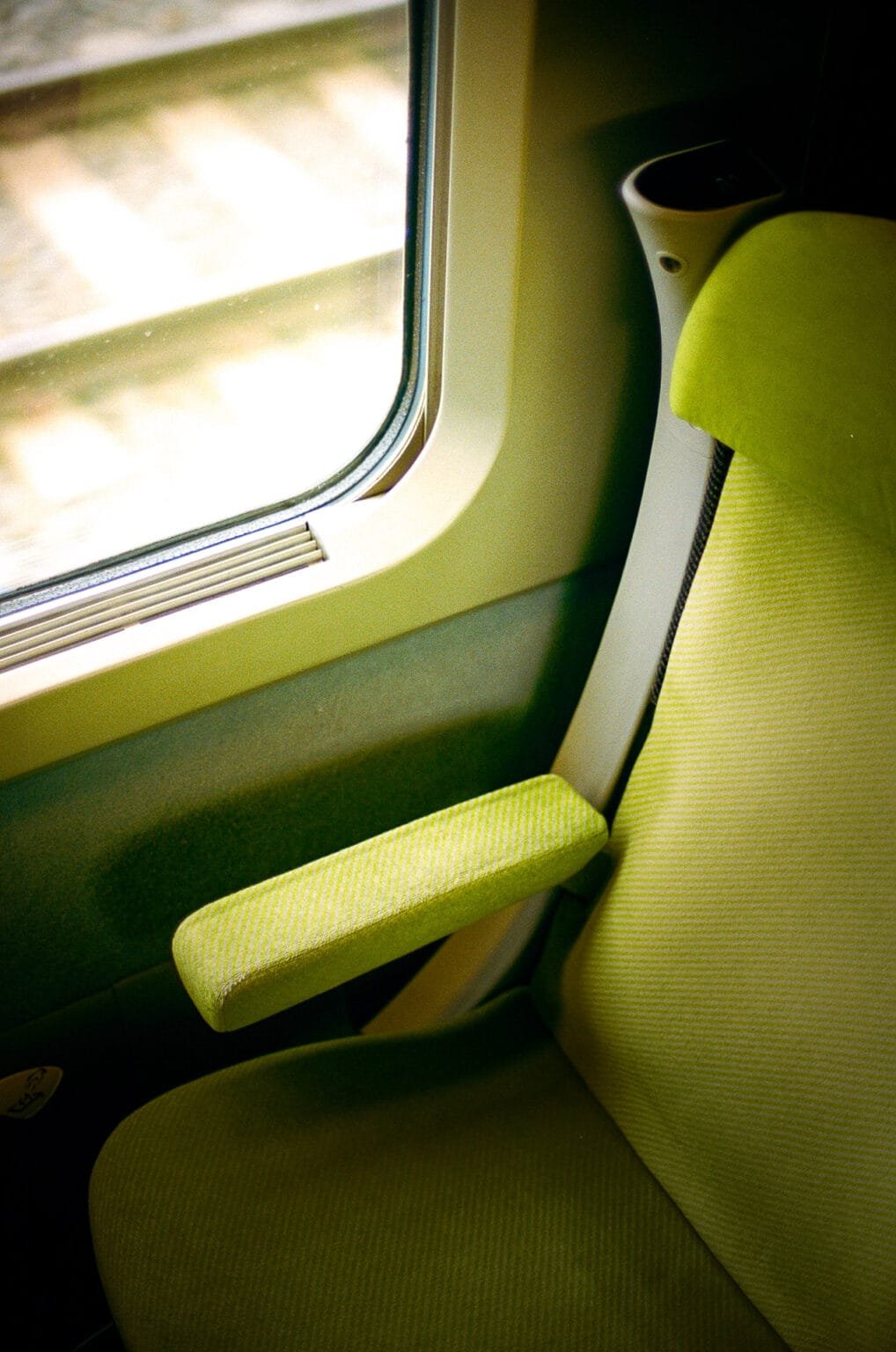 Siège vert d’un TGV vu en gros plan, avec la voie ferrée visible à travers la fenêtre.
