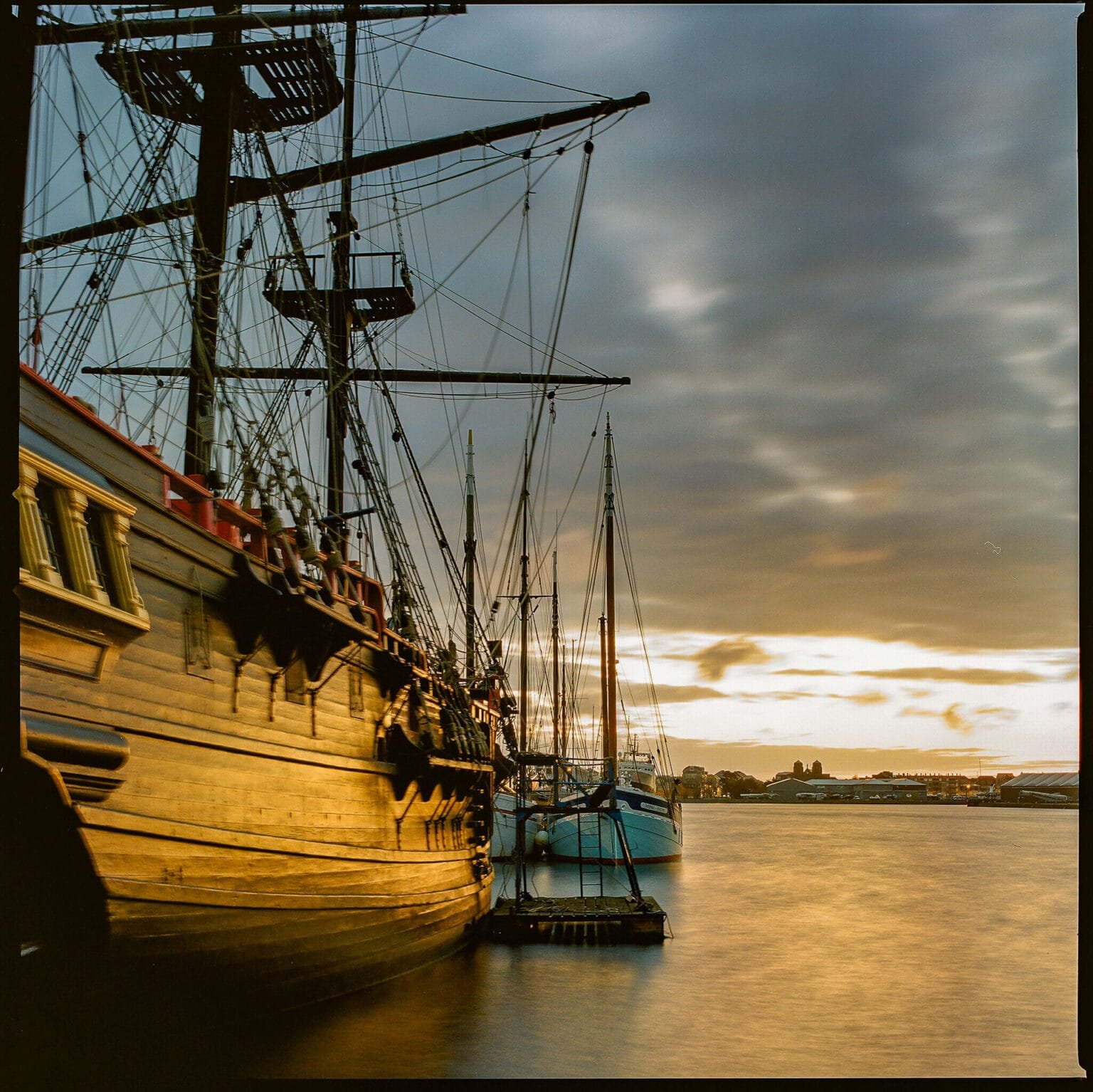 Trois-mâts amarrés dans le port de Saint-Malo au coucher du soleil, la coque en bois baignée de lumière dorée.