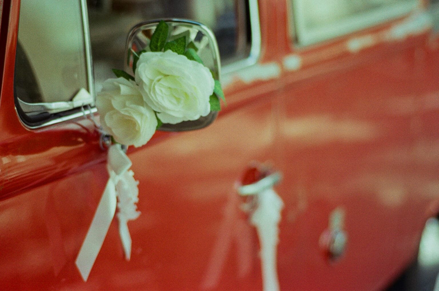Rétroviseur d’un VW Combi rouge décoré de fleurs blanches et de rubans pour un mariage, garé près de la mairie de Nantes.