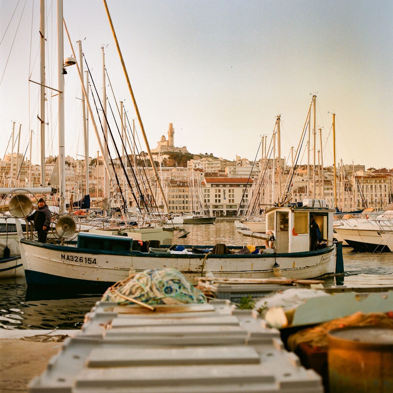 Bateau de pêche rentrant au Vieux-Port de Marseille à l’aube, avec Notre-Dame-de-la-Garde en arrière-plan.