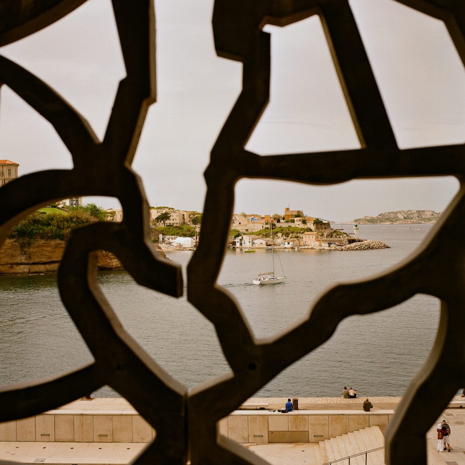 Voilier naviguant près du Mucem à Marseille, vu à travers la dentelle architecturale du musée, photographié avec un Hasselblad 500 C/M et une pellicule Kodak Gold 200.