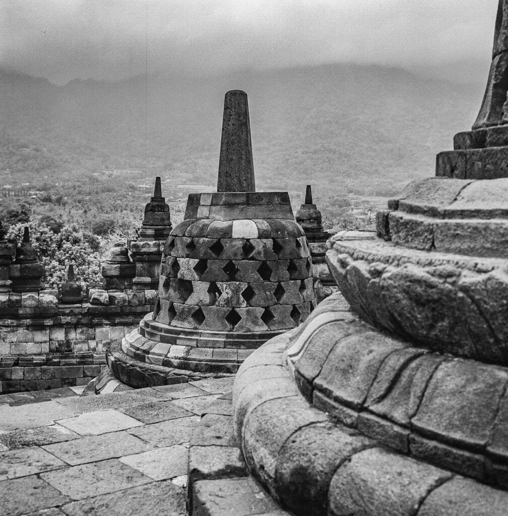 Stûpa en pierre du temple de Borobudur, photographié en noir et blanc sur fond de montagne brumeuse.