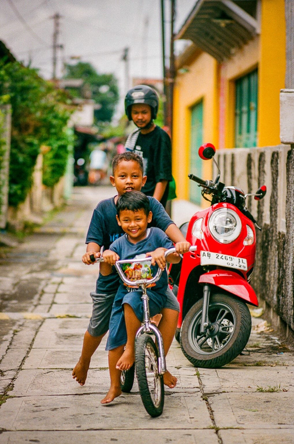 Deux jeunes garçons souriants sur un vélo dans une ruelle de Yogyakarta, près du Kraton.